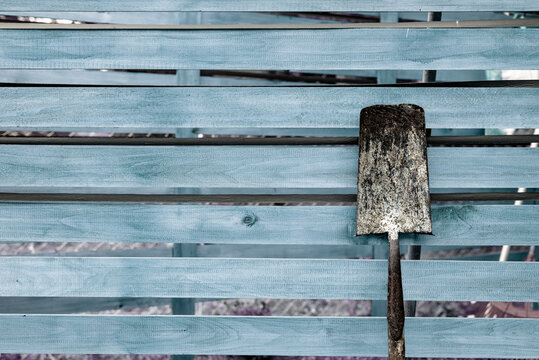 a rusty shovel leaning on a old wooden fence