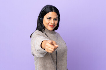 Young latin woman woman isolated on purple background listening music and pointing to the front