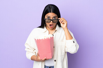 Young latin woman woman isolated on white background surprised with 3d glasses and holding a big...