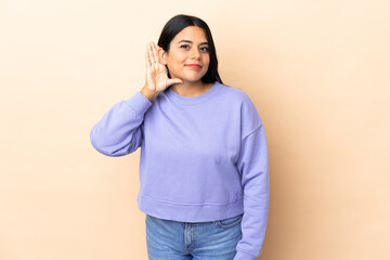 Young latin woman woman over isolated background listening to something by putting hand on the ear