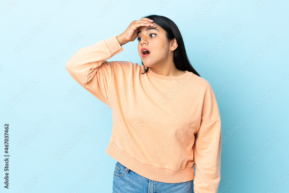 Wall mural Young latin woman woman isolated on blue background doing surprise gesture while looking to the side