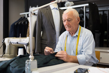Naklejka na ściany i meble Elderly tailor sews lapel to a jacket in his workshop