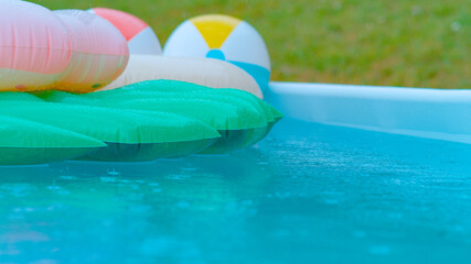 CLOSE UP: Backyard pool filled with floaties getting caught in autumn rainstorm.