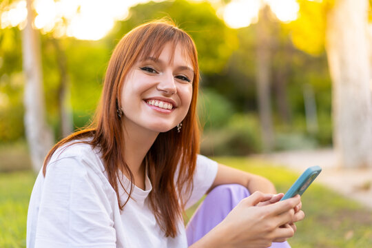 Young pretty redhead woman at outdoors using mobile phone with happy expression