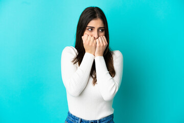 Young caucasian woman isolated on blue background nervous and scared putting hands to mouth