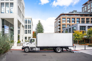 Profile of day cab medium size semi truck with long box trailer unloaded delivered goods to new multi-level apartments in unban city area