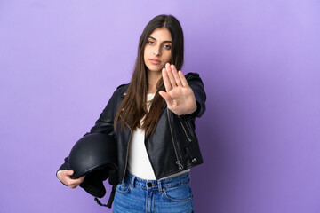 Young caucasian woman with a motorcycle helmet isolated on purple background making stop gesture