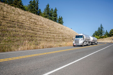 White day cab big rig semi truck transporting hazardous liquid cargo in two tank semi trailers...