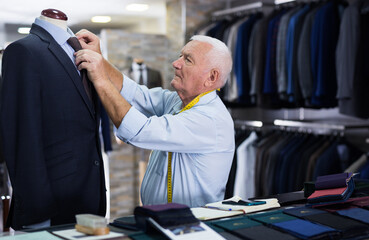 Mature male tailor takes measurement from his jacket using a measuring tape