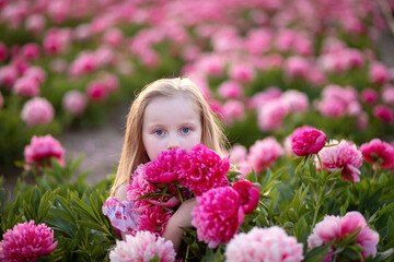 Little beautiful girl in a peony field on sunset background.