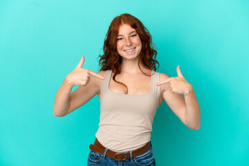 Teenager reddish woman isolated on blue background proud and self-satisfied