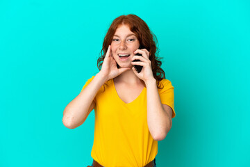 Teenager reddish woman using mobile phone isolated on blue background with surprise and shocked facial expression