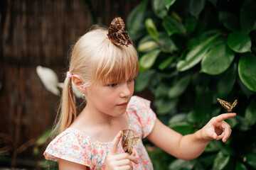 portrait of a little blonde girl with live beautiful butterflies in the park. Butterflies sit on the head, hands. Amazing nature, happy childhood.