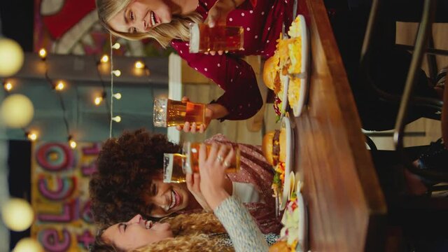 Vertical video of group of multi-cultural female friends sitting at table eating meal and enjoying girls night out together- shot in slow motion