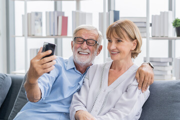 Happy husband and wife senior couple elderly family, caucasians mature, adult lover and retired man, woman using smartphone selfie on cozy sofa, couch at home together. Comfortable, relax people.