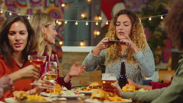Woman taking photo of food to post on social media as multi-cultural group of friends enjoy night out in restaurant together - shot in slow motion