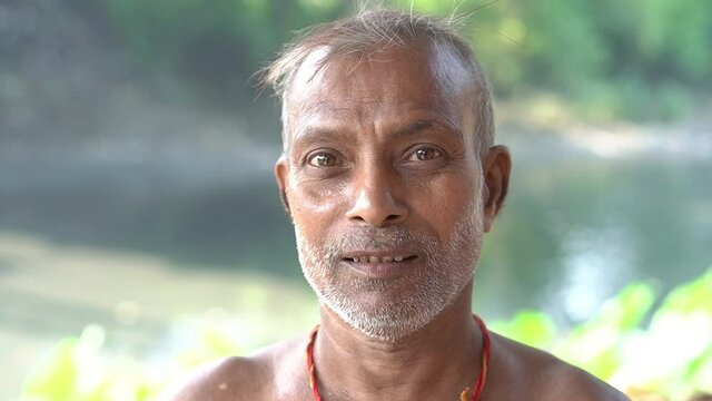 Head shot of a senior potter artist standing near a river, busy in making terracotta elephant, a traditional doll of Panchmura Bankura, used as home interior as well as Hindu religious purpose.