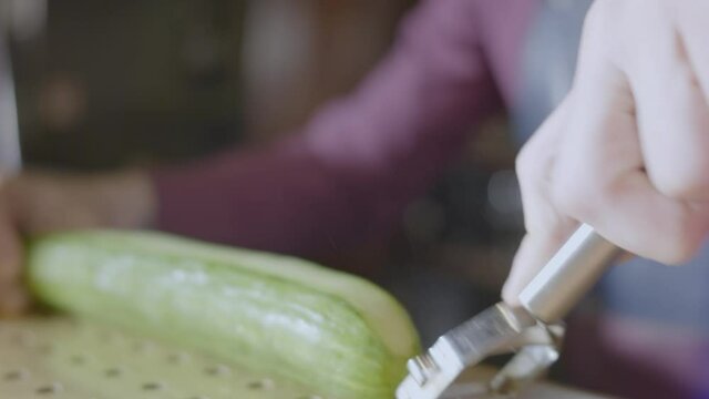 A bartender prepares his garnish using a cucumber