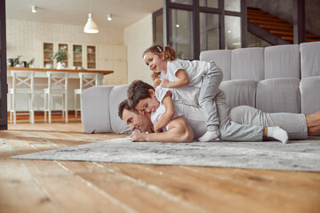 Low angle of jolly son and daughter on dad back while he is lying on floor during training at home