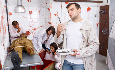 Portrait of focused guy with friends in escape room stylized as medical room with traces of blood