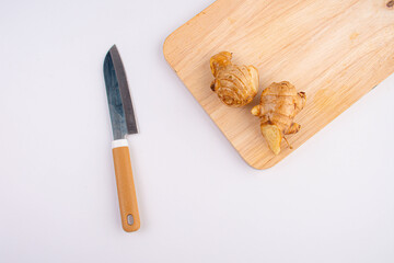 Fresh ginger and knife on a wooden chopping board on table white background 