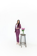 a business woman psychologist in a red suit stands in the center of the frame on a white background next to a table with flowers