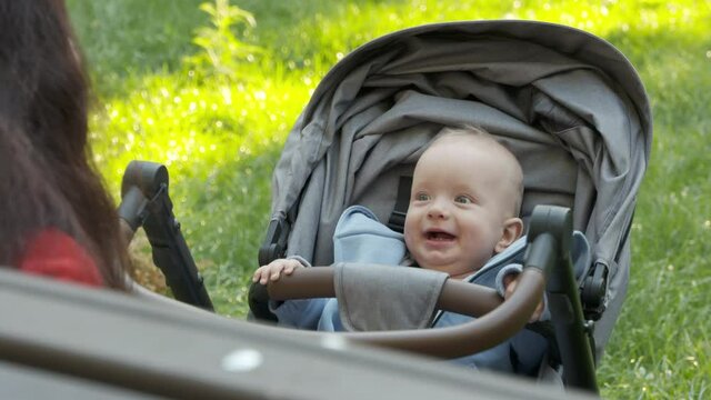 Happy baby boy in stroller outdoors, smiling face of six month old infant in the park on a summer day. High quality 4k footage