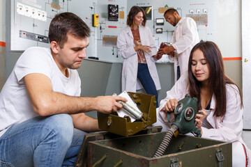 Young friends solving conundrum in quest room in view as closed nuclear bunker, inspecting box with...
