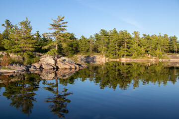 Fototapeta na wymiar Pinetree reflecting in the water along the rocky shore of Franklin Island on Georgian Bay on a calm summer day