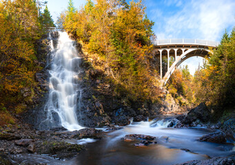 A bridge crosses the river as a waterfall flows into it in autumn