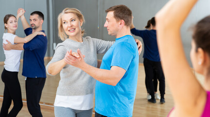 Smiling mature woman enjoying slow foxtrot in dance studio for adults..