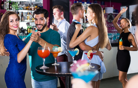 Young smiling women with men are dancing in pairs on the dance floor in the nightclub