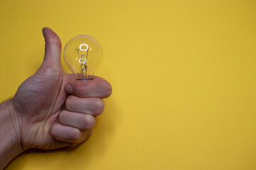 Incandescent light bulb in man's hand on yellow background with copy space, flat lay, ideas concept. space for text
