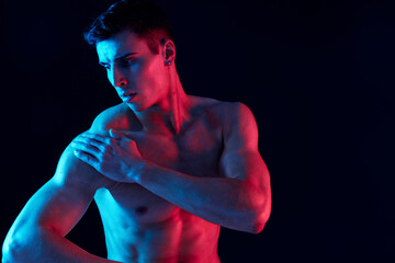 sexy athletes with pumped up muscles of the arms looks to the side on a black background and neon...