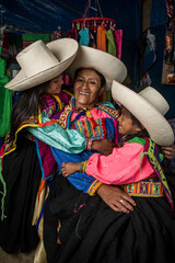 Mujer madre latinoamericana andina haciendo hilo de lana de oveja y enseñando el telar de cintura a sus hijas.