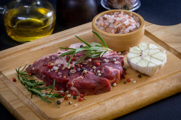 Raw steak and ingredients on a dark wooden cutting board
