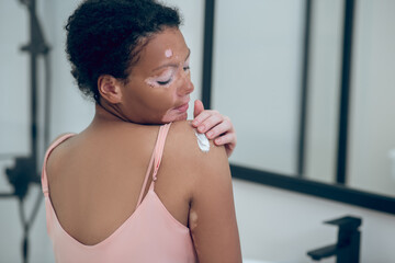 A cute woman applying cream on her body