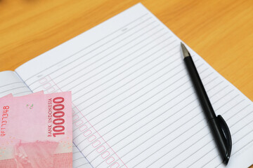 Empty book with pen and paper money above the table. Closeup