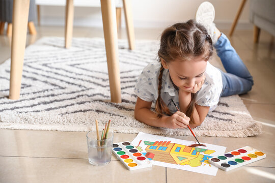 Little girl painting with watercolor paints on floor at home