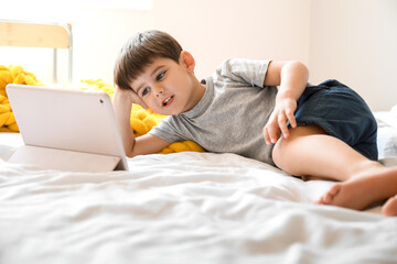Little boy watching cartoons on tablet computer in bedroom