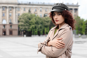 Portrait of young woman in leather cap holding her shoulders on city square
