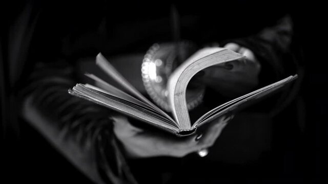 Hands of witch woman turns over pages of old paper book at night background. Beautiful scene. Education, science, magic, halloween cosplay concept. Black and white