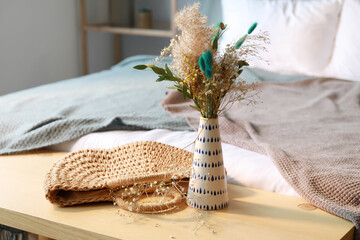 Vase with beautiful bouquet of dried flowers and wicker bag on wooden table in bedroom