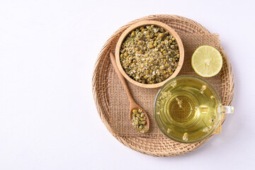 Chamomile tea in a cup glass with dried chamomile flowers in a bowl and spoon on white background, Healthy herbal tea