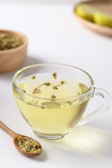 Chamomile tea in a cup glass with dried chamomile flowers in a spoon on white background, Healthy herbal tea