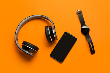 Modern headphones, mobile phone and smart watch on orange background