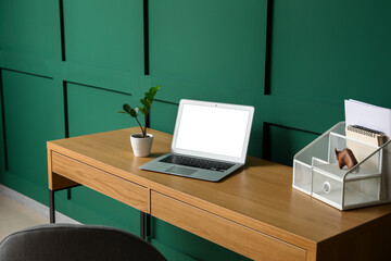 Fototapeta premium Modern laptop, houseplant and organizer on wooden table near color wall