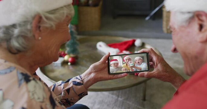 Senior caucasian couple using smartphone for christmas video call with smiling family on screen