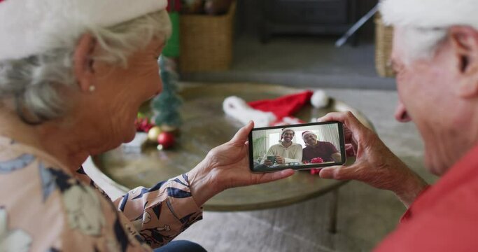 Senior caucasian couple using smartphone for christmas video call with smiling family on screen