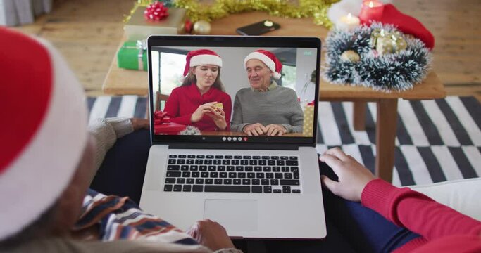 African american mother and daughter using laptop for christmas video call with family on screen